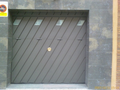 Porta Basculant amb xapa llisa en diagonal doblegada amb detall de vidres